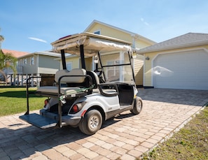 Une voiturette de golf est garée sur une allée pavée devant une maison d’habitation avec un garage.