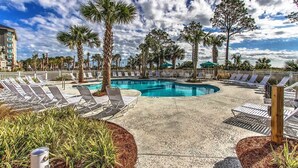 A pool area with lounge chairs, palm trees, and a building in the background. - Ocean Dunes by Hilton Head Retreats (Hilton Head Island)