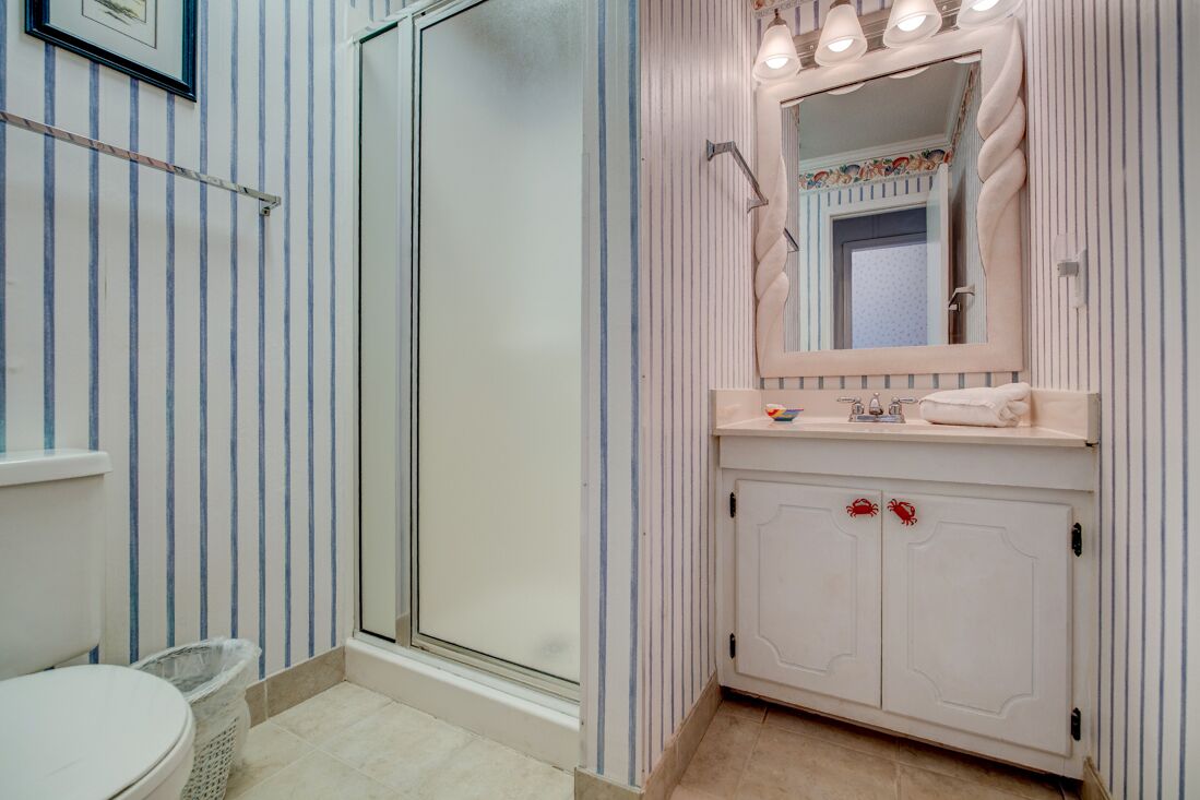 Une salle de bain avec un papier peint à rayures, un lavabo blanc avec un miroir et une porte de douche.