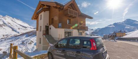 A building with a sign indicating it is a ski resort, a parked car, and snow-covered mountains in the background.