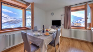 A dining area with a table set for two, a television, and a view of snowy mountains. - Fiocco Di Neve Ski in- Ski out Mt.10 (Livigno)