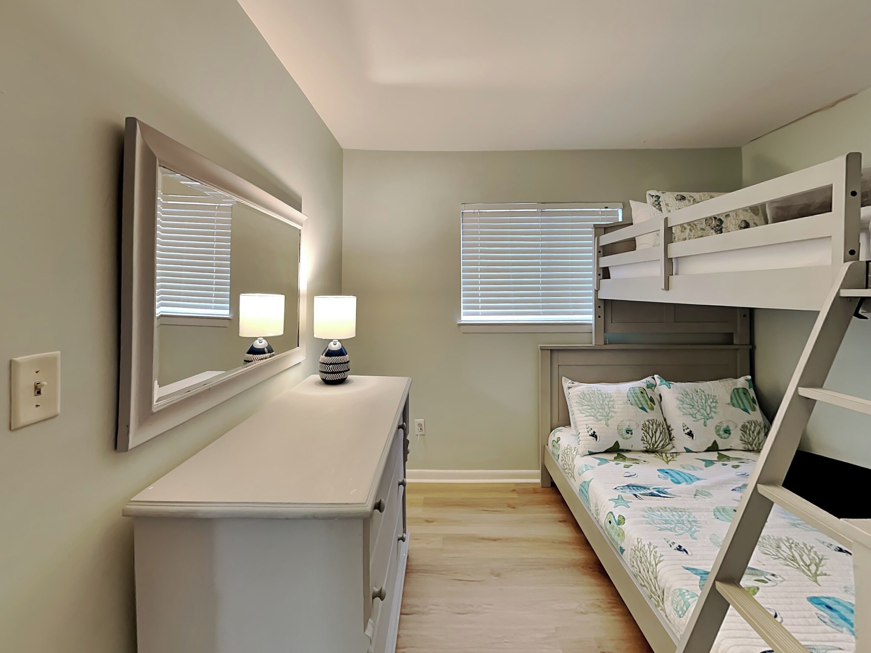 A bedroom with a bunk bed, a dresser, a mirror, and a window with blinds.