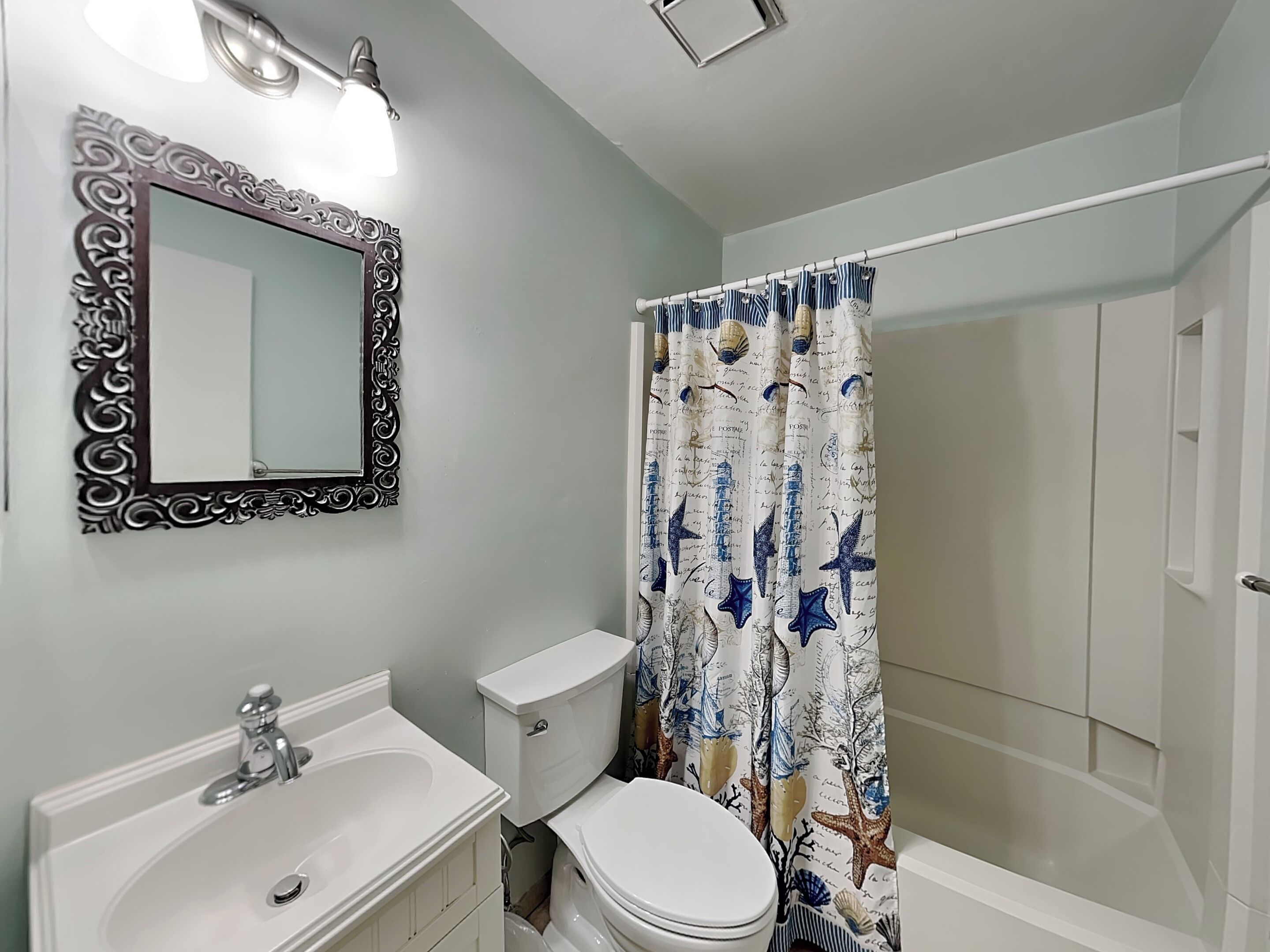 A bathroom with a white sink, toilet, and shower curtain with a nautical theme.