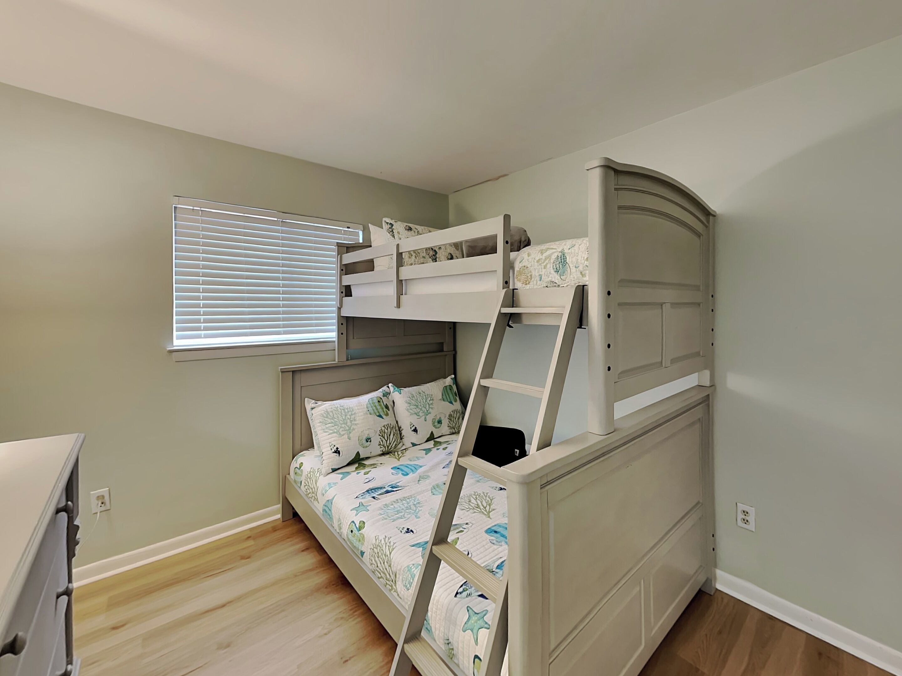 A bunk bed with a ladder, a window with blinds, and a wooden floor.