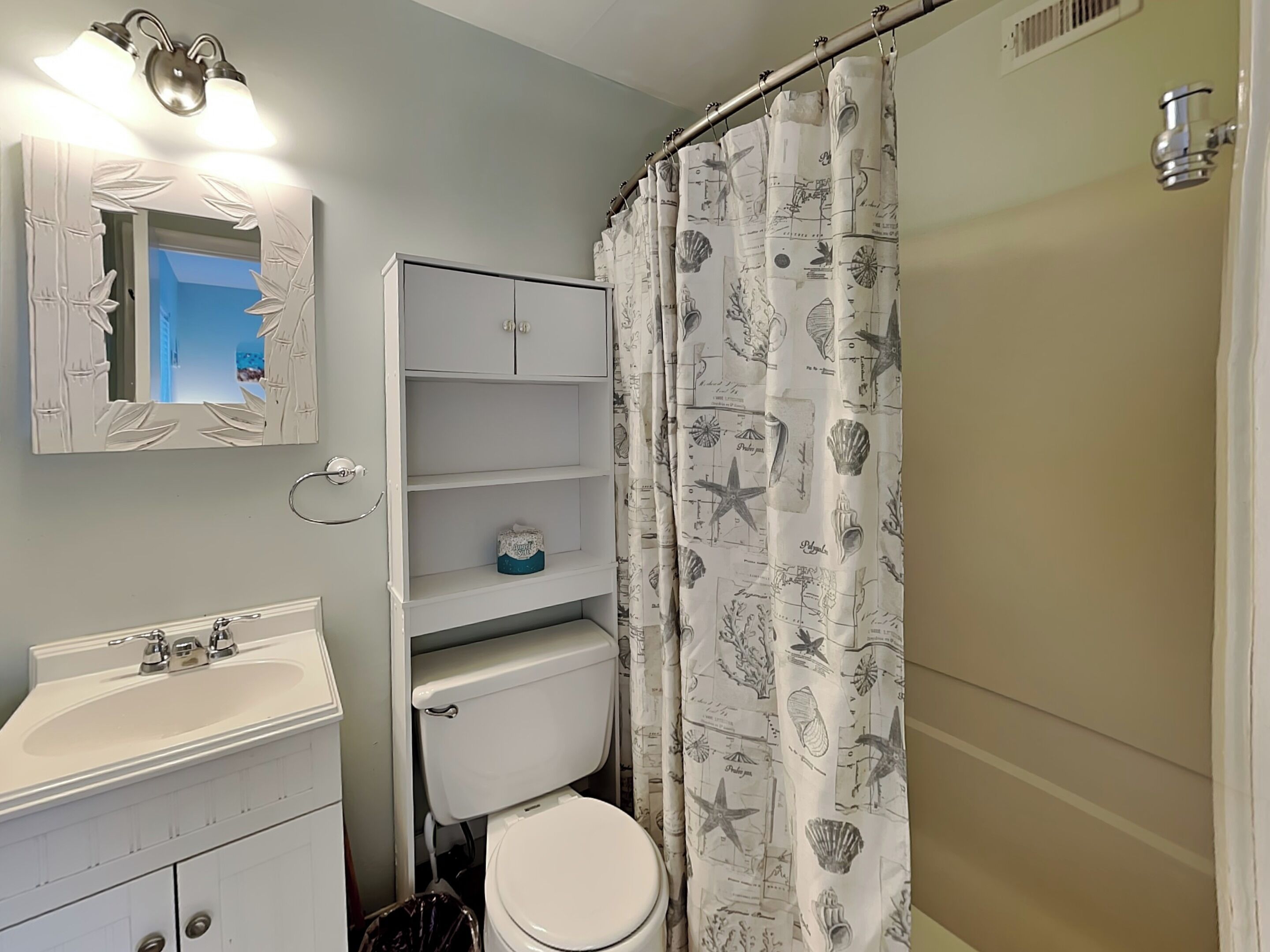 A bathroom with a toilet, sink, mirror, and shelves.