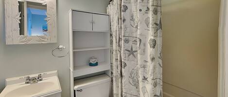 A bathroom with a toilet, sink, mirror, and shelves.