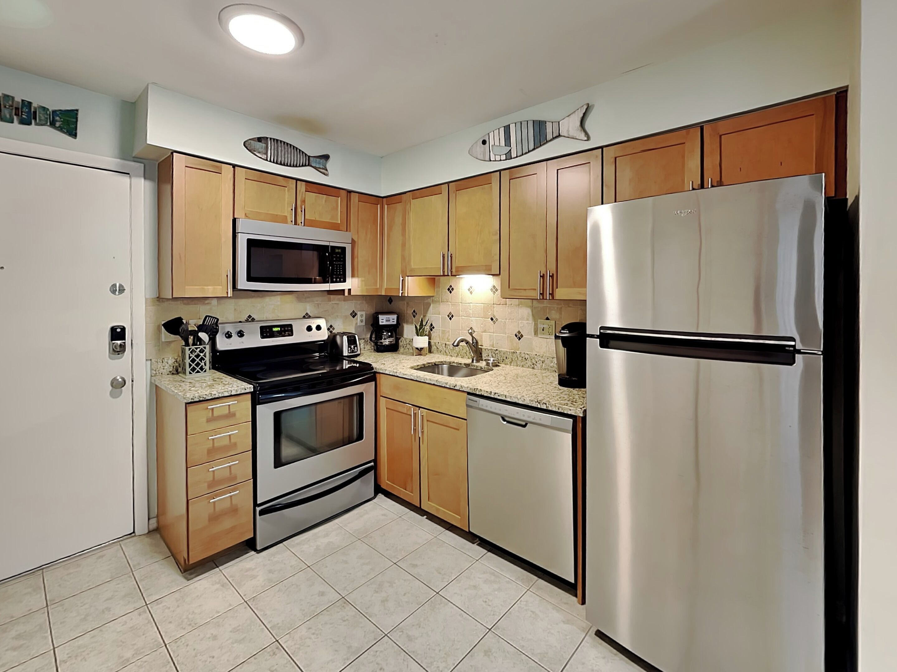 A compact kitchen with a microwave, stove, refrigerator, and wooden cabinets.
