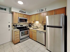 A compact kitchen with a microwave, stove, refrigerator, and wooden cabinets. - Fiddler's Cove by Hilton Head Retreats (Hilton Head Island)