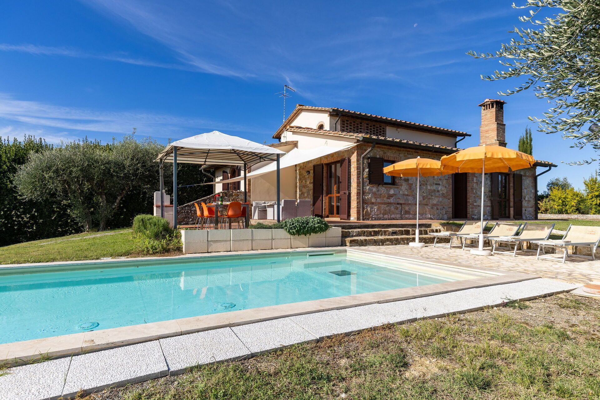 A poolside area with a covered seating area, outdoor umbrellas, and lounge chairs.