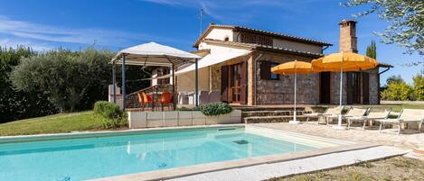 A poolside area with a covered seating area, outdoor umbrellas, and lounge chairs.