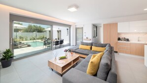 A modern living room with a grey sofa, a wooden coffee table, and a glass sliding door leading to a pool area.