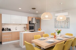 Une cuisine moderne avec des meubles blancs, un îlot central et un coin repas agrémenté de chaises jaunes et d’une table en bois.
