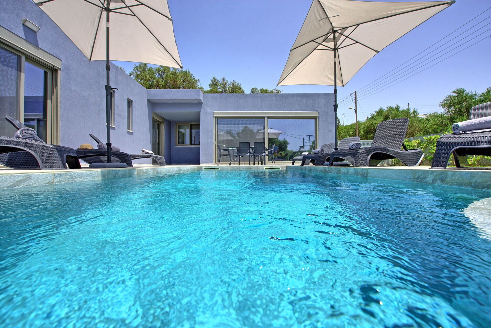 Une piscine entourée de chaises longues et de parasols, le tout adossé à un bâtiment moderne doté de grandes fenêtres et de grandes portes.