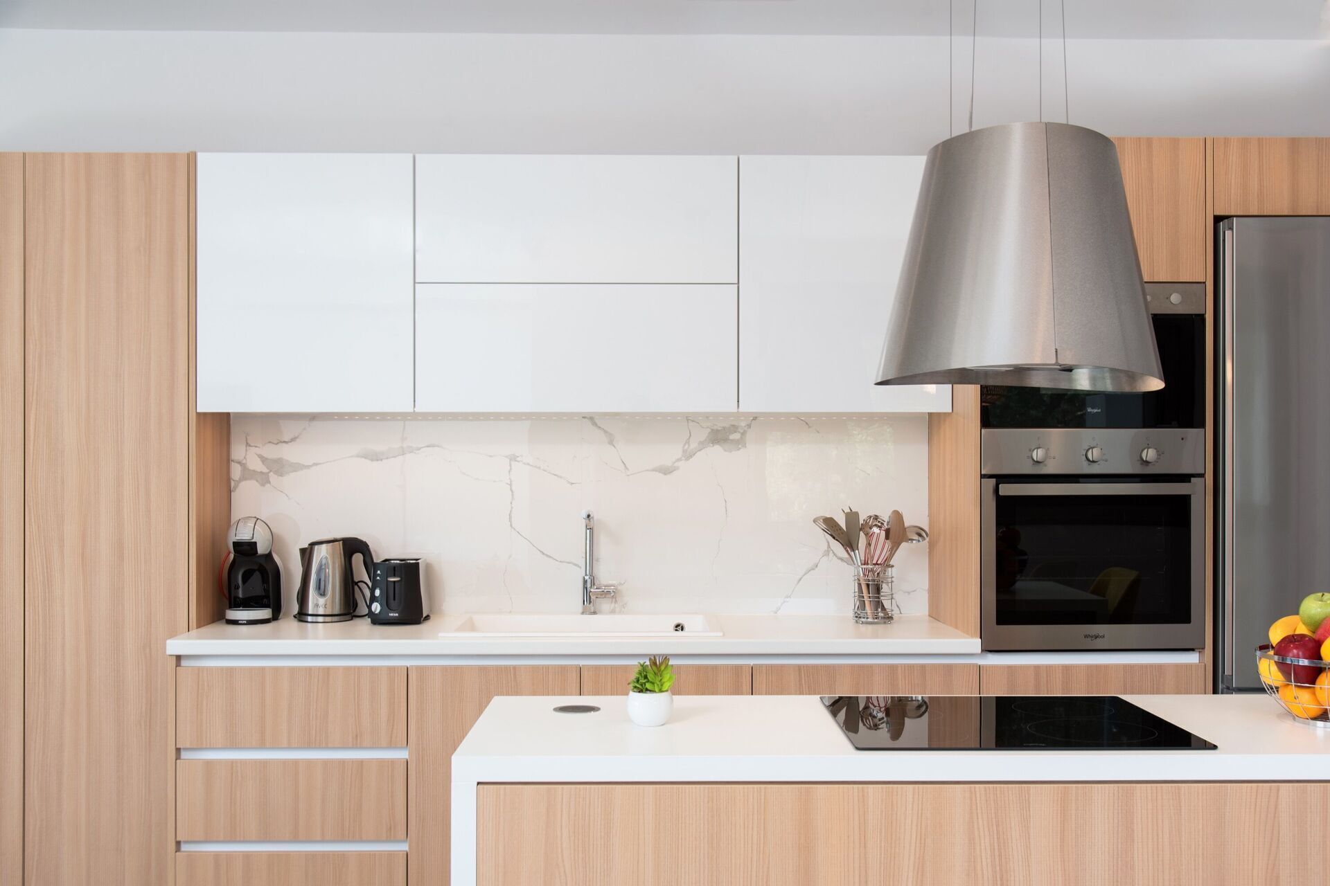Une cuisine moderne avec des armoires blanches, un dosseret en marbre, une hotte de cuisinière en acier inoxydable, un four encastré et une plaque de cuisson à induction noire.