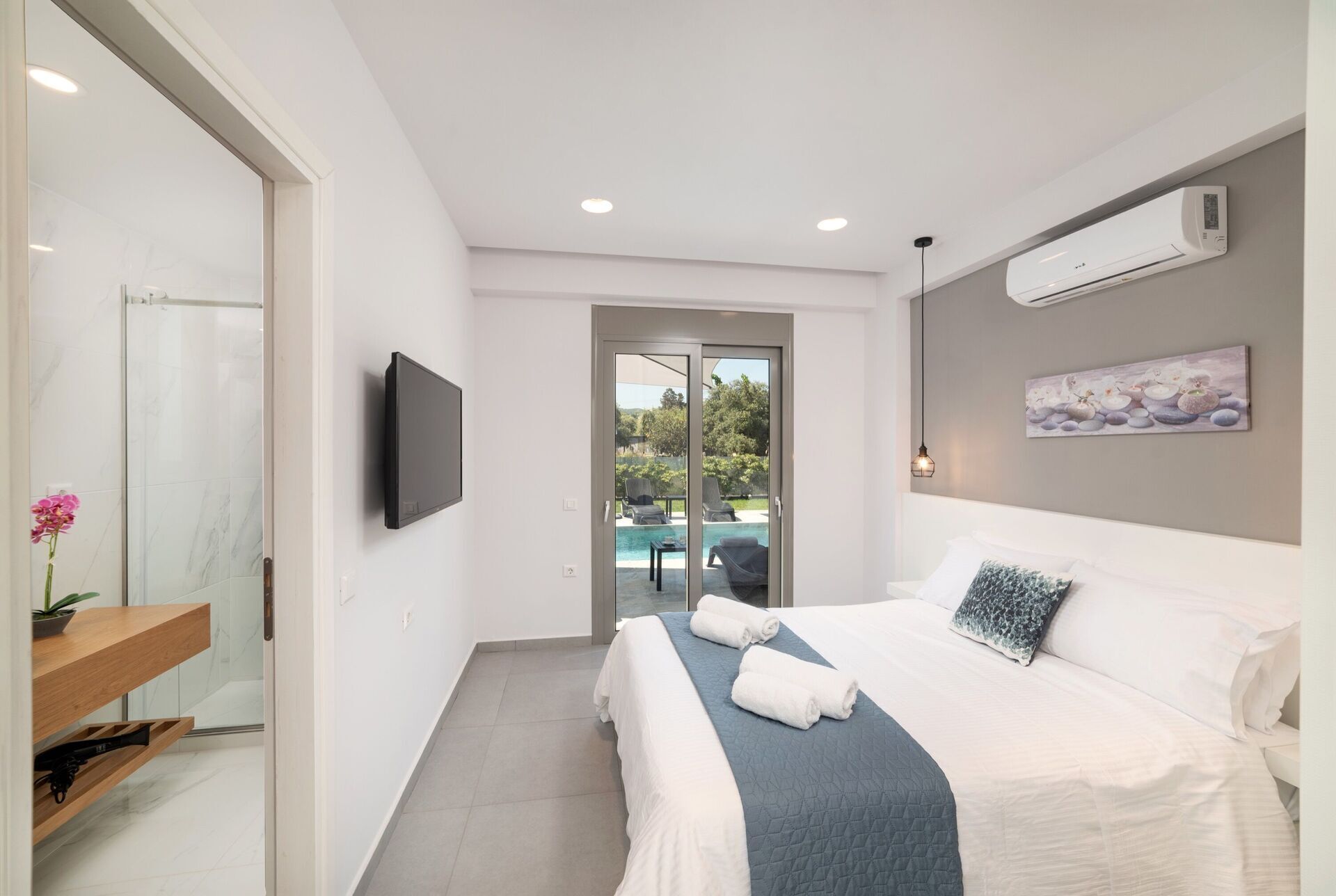 A modern bedroom with a bed, a TV, an air conditioner, and a view of an outdoor pool.