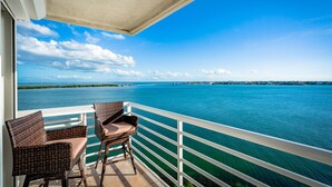 Een balkon met rieten stoelen en uitzicht op een groot wateroppervlak.