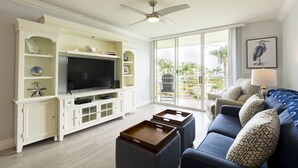 Een woonkamer met een televisie, witte kasten, een blauwe bank en een balkon met uitzicht.