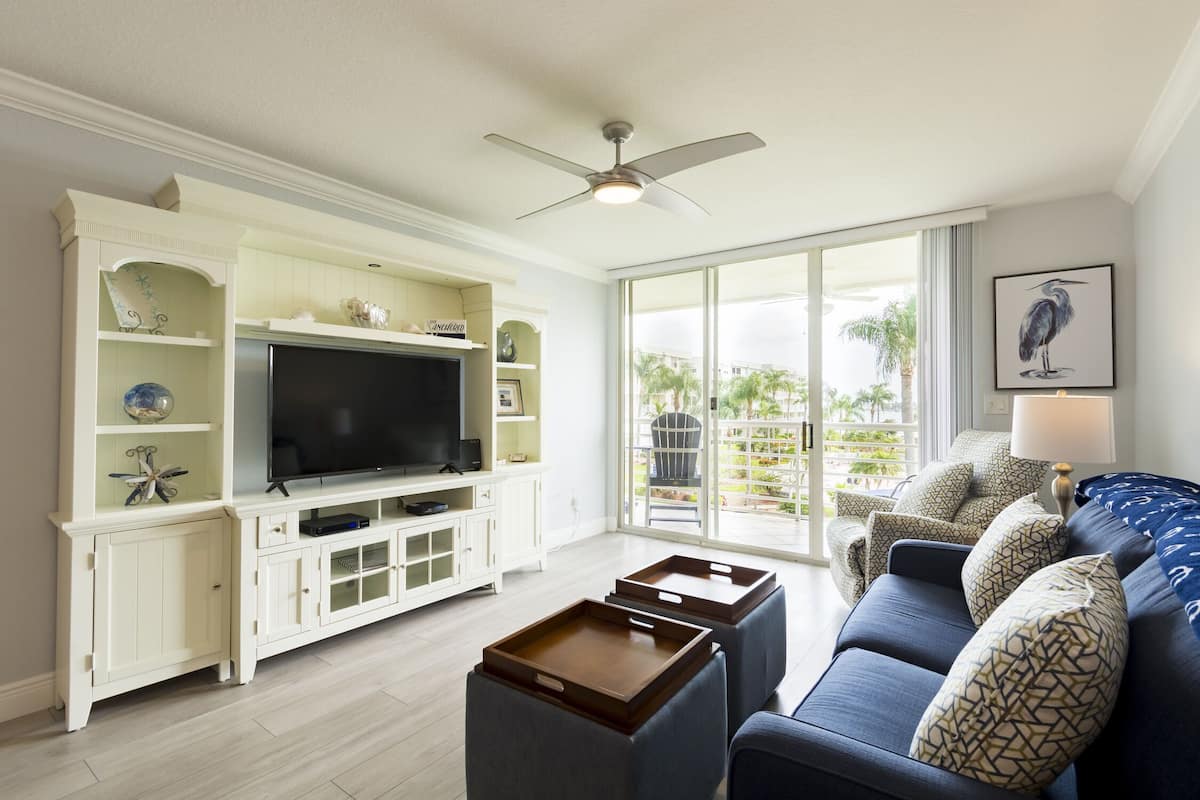 Un salón con televisor, muebles blancos, sofá azul y un balcón con vistas.