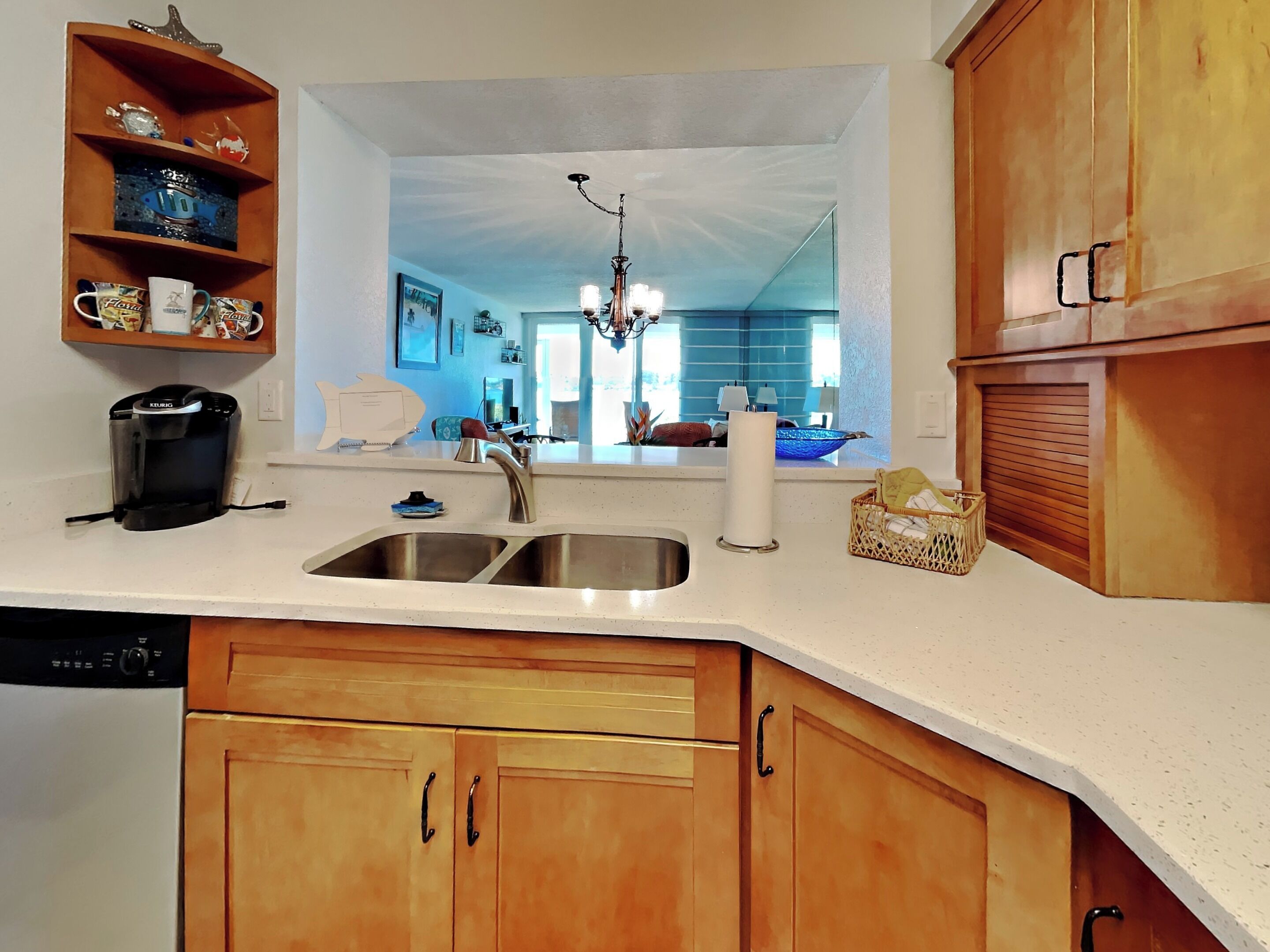 Una cocina con armarios de madera, una cafetera, un lavabo y un espejo que refleja la habitación.