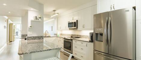 A modern kitchen with white cabinets, stainless steel appliances, granite countertops, and a built-in oven.