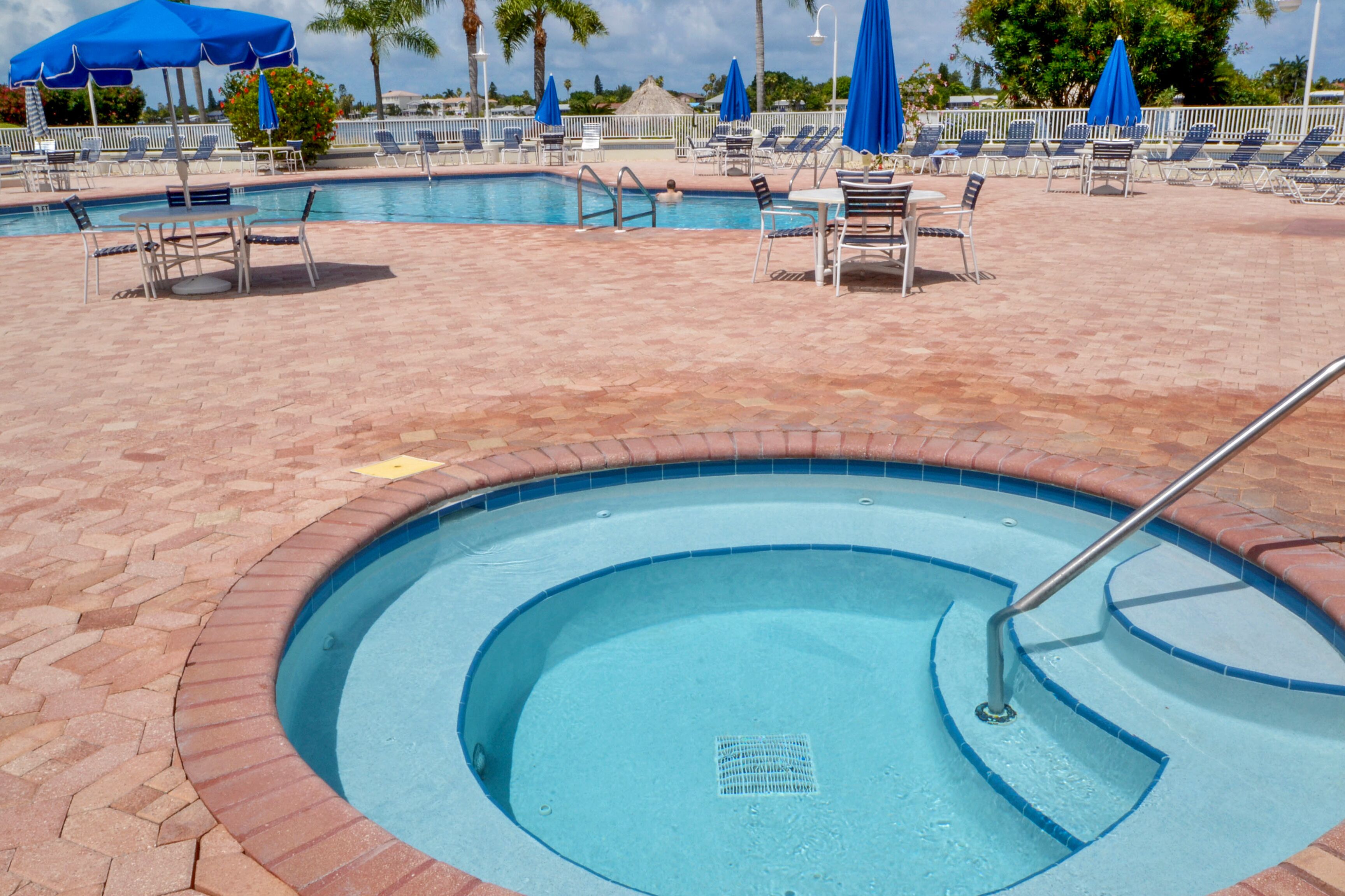 A swimming pool with a brick border, lounge chairs, and blue umbrellas.