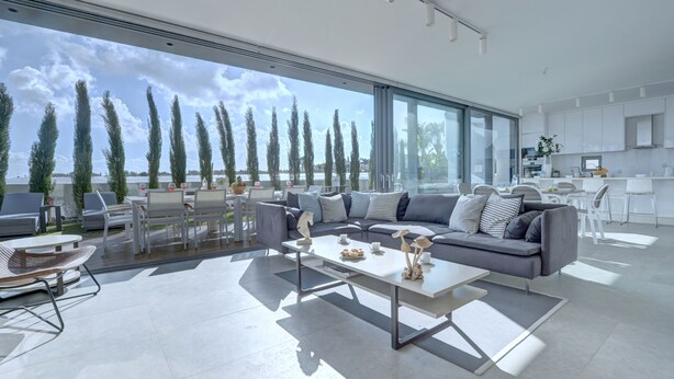 A modern living room with a large window, a grey sofa, and a dining area. - Protaras Holiday Villa Wp8 (Paralimni)