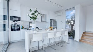 A modern kitchen with white cabinetry, stainless steel appliances, and a central island with bar stools. - Protaras Holiday Villa Wp8 (Paralimni)