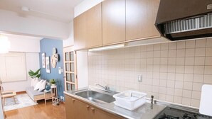 A kitchen with a stove, sink, and cabinets. There is a basket on the counter and a plant in the corner. - OUCHI HOTEL Hijiyama (Hiroshima)