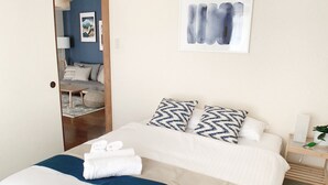 A neatly made bed with white and blue bedding, a wooden nightstand with a plant, and a framed artwork on the wall. - OUCHI HOTEL Hijiyama (Hiroshima)