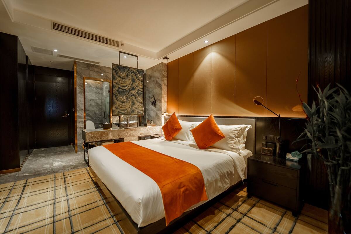 Ein modernes Hotelzimmer mit einem großen Bett, einem Nachttisch, einem Spiegel und Blick auf die Stadt.