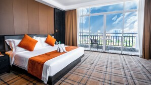 A hotel room with a large bed, a nightstand, a window with a view of buildings, and a balcony. - Ocean Hotel (Phnom Penh)