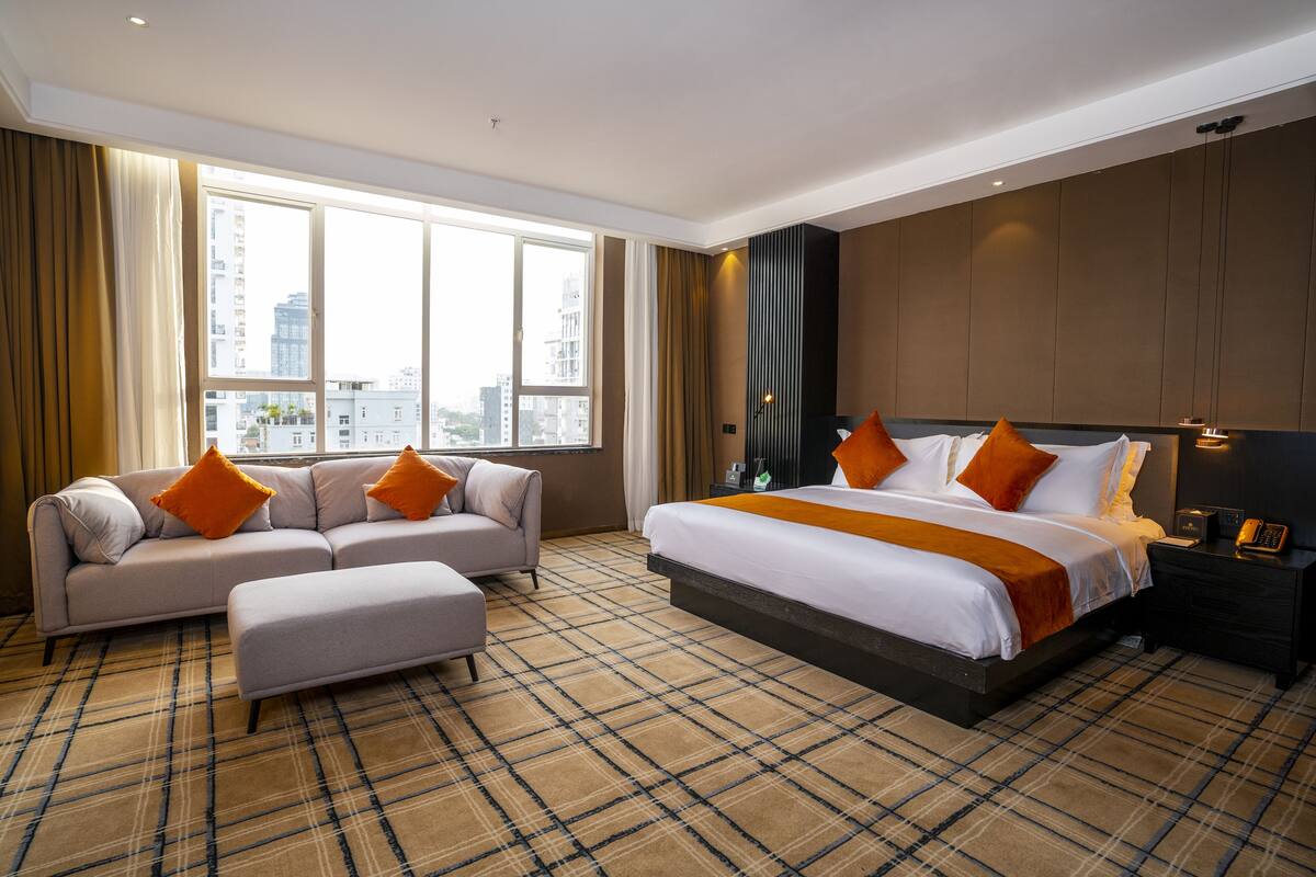 Ein Hotelzimmer mit einem großen Bett, einer Schlafcouch, einem Hocker und Blick auf die Stadt durch große Fenster.