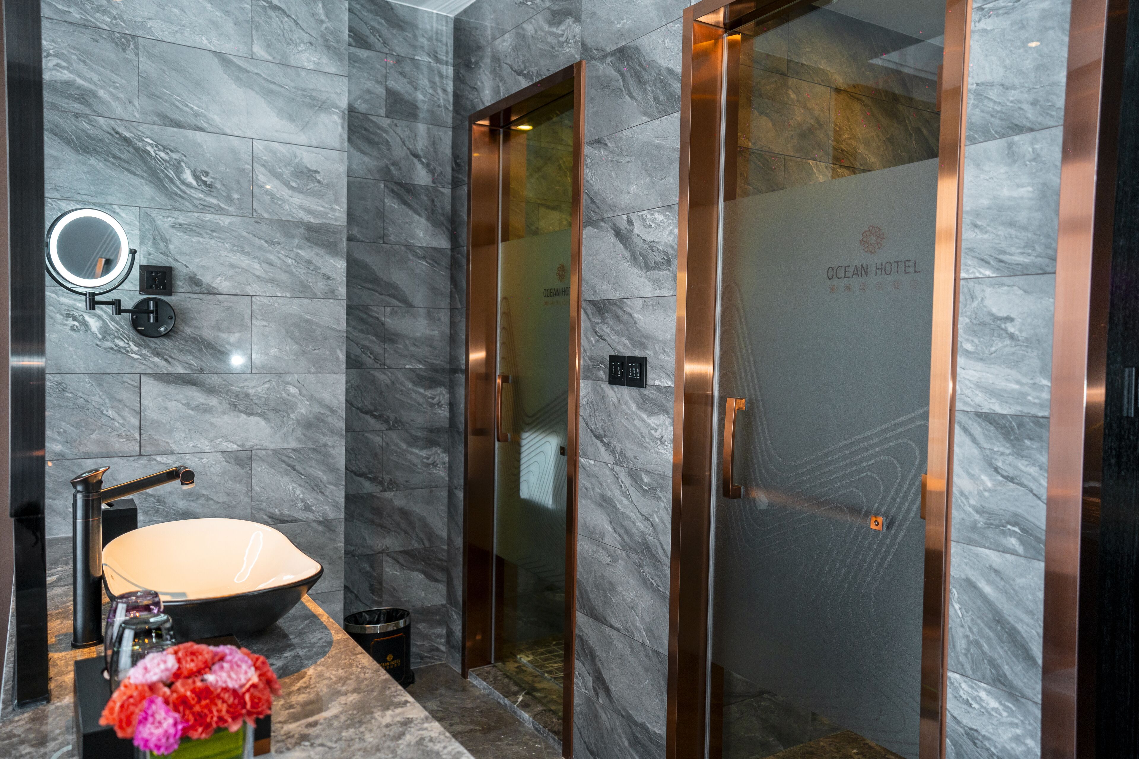 A modern bathroom with a marble floor, a sink, a mirror, and a glass-enclosed shower area.