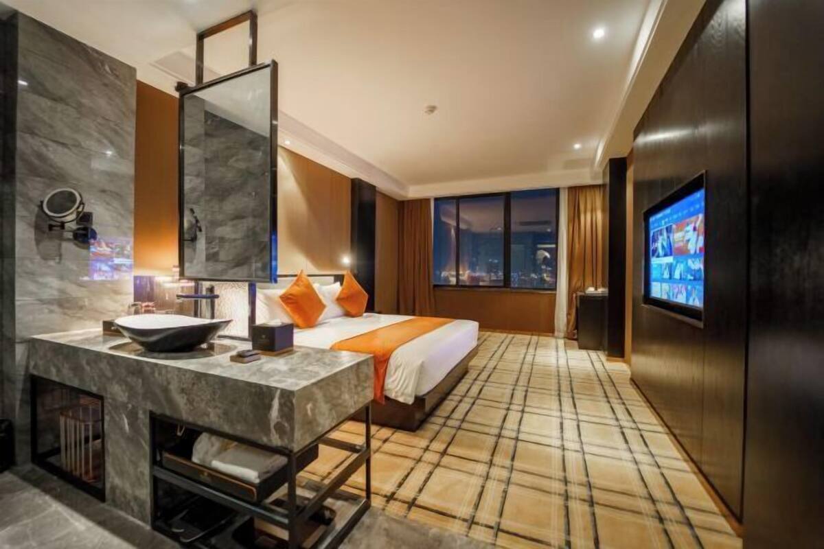 Ein modernes Hotelzimmer mit einem großen Bett, einem Fernseher, einem Badezimmer mit Marmorwaschbecken und Blick auf die Stadt.