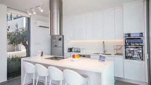 A modern kitchen with white cabinetry, a stainless steel range hood, and a central island with bar stools. - Protaras Holiday Villa Wp4 (Paralimni)