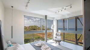 A modern bedroom with a large bed, a seating area, and a balcony with a view of the landscape. - Protaras Holiday Villa Wp4 (Paralimni)