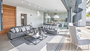 A modern living room with a grey sofa, coffee table, and pendant lights. A spiral staircase is visible in the background. - Protaras Holiday Villa Wp4 (Paralimni)