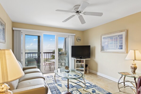 A living room with a ceiling fan, a flat-screen TV, a sofa, a coffee table, and a view of the outdoors through a sliding glass door.