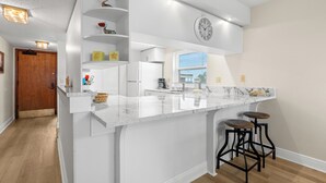A kitchen with a white marble countertop, a clock, and two bar stools.