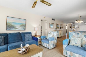 Een woonkamer met een bank, fauteuil, salontafel en een schilderij van een strandgezicht.