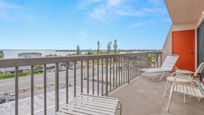 A balcony with a view of a road and water, white metal chairs, and a door.