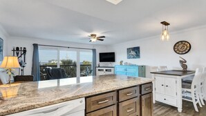 A modern kitchen with a granite countertop, wooden cabinets, a ceiling fan, and a dining area with a table and chairs. - 🌅 Gulf Gate Resort Unit 206 – Updated Bay View Condo with Coastal Charm for Up to 4 Guests (St Pete Beach)