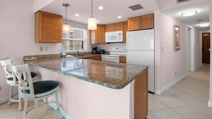 A kitchen with granite countertops, wooden cabinets, a white refrigerator, and a built-in microwave. - 🌅 Gulf Gate Resort #508 – Dual Water Views & Coastal Comfort (St Pete Beach)