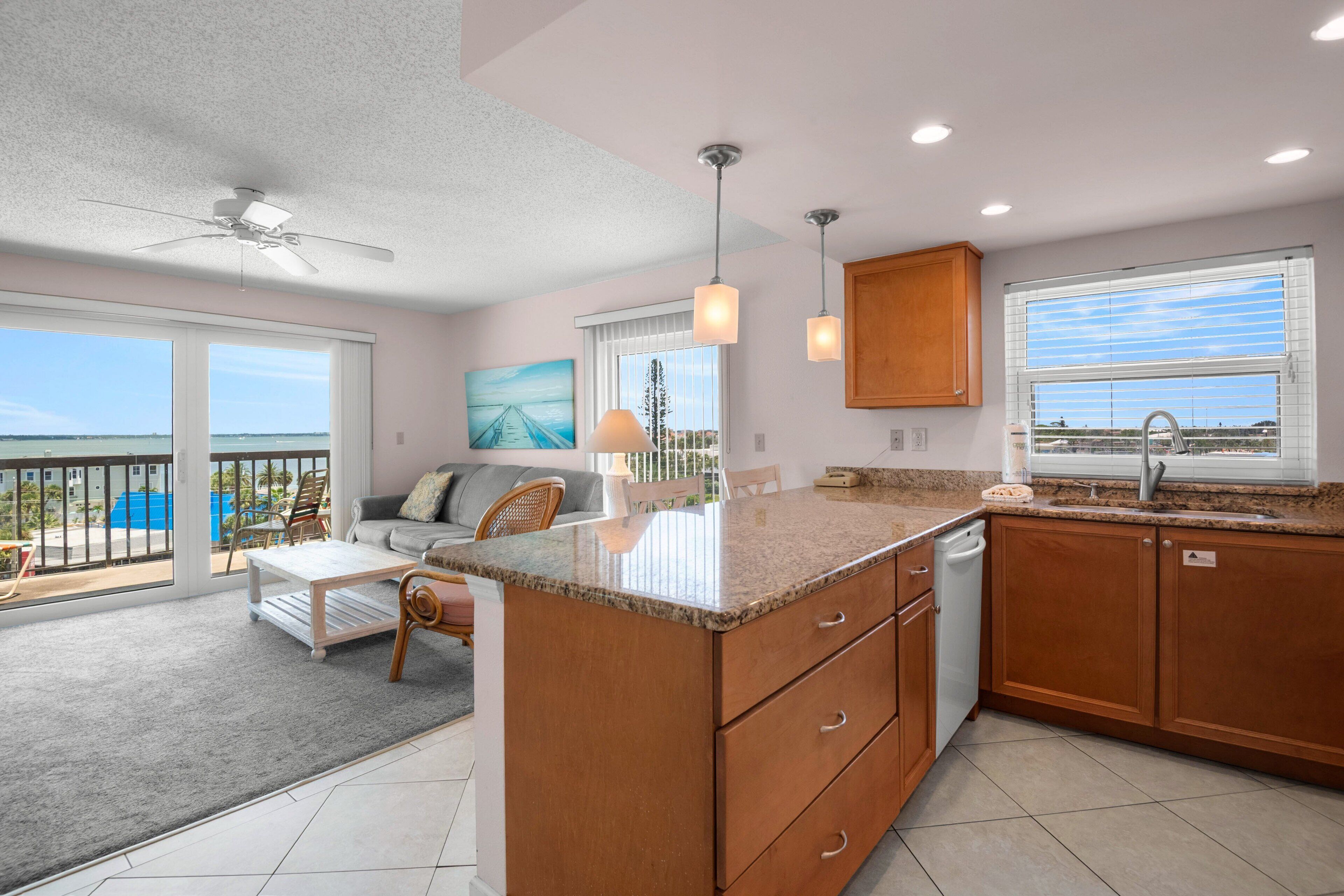 A spacious living area with a large island, a balcony with a view, and a kitchen with wooden cabinets and a window.