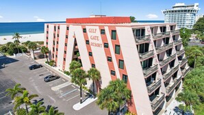 A multi-story hotel with balconies, a parking lot, and a beach view. - 🌅 Gulf Gate Resort #508 – Dual Water Views & Coastal Comfort (St Pete Beach)