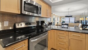 A modern kitchen with stainless steel appliances, wooden cabinets, and a black countertop. - 🌅 Unit 102 at Gulf Gate – Renovated Luxury with Gulf Views for Up to 6 Guests (St Pete Beach)