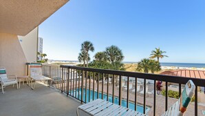 A balcony with a pool, lounge chairs, and a view of the beach. - 🌅 Unit 102 at Gulf Gate – Renovated Luxury with Gulf Views for Up to 6 Guests (St Pete Beach)