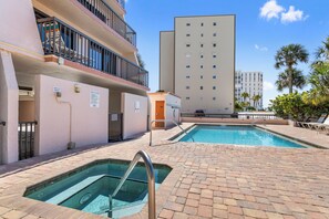 A pool area with two pools, a building with a balcony, and a palm tree in the background.