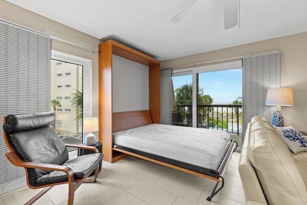 A hotel room with a bed, a chair, a sofa, a balcony with a view, and a window with blinds. - 🌴 Gulf Gate Resort Unit 201 – Updated 1BR Condo with Gulf Views & Premium Comfort (St Pete Beach)