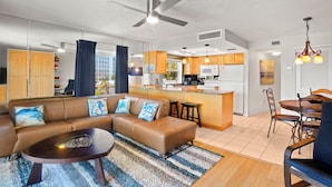 A modern living room with a brown leather sofa, a coffee table, and a dining area with wooden chairs and a table. - 🌅 Gulf Gate Resort Unit 208 – Dual-Balcony Water View Condo for Up to 4 Guests (St Pete Beach)